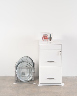 Coca-Cola can and hand grenade in cast acrylic on top of a metal filing cabinet next to aluminum trash can lids in a metal crate